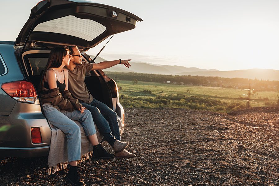 Insurance Quote - Young Couple Sitting in the Trunk of Their Car On a Road Trip Enjoying the Views of the Countryside at Sunset
